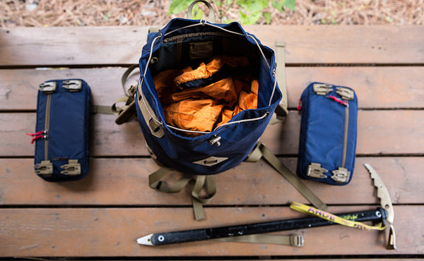 An above-shot of the Guide's Pack open to reveal its contents, with a few acccessories laid beside it.